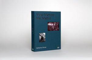 A dark teal, cloth-bound hardcover book titled Мир Метро / Mir Metro by Katharina Gruzei stands against a light grey background. The cover features two inset images: a smaller, black-and-white photo of a person on an escalator, and a larger color photo of red marbled stone with light reflections.