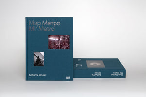 A studio shot of two hardcover books with dark teal cloth covers, titled Мир Метро Mir Metro by Katharina Gruzei in silver text. One book stands vertically, showing its cover with two inset photos of subway scenes. The other book lies horizontally, displaying its spine against a plain white background.