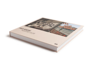 A hardcover copy of the photography book Fred Herzog: Modern Color is displayed at an angle on a white background. The book has a thick spine and a pale beige cover featuring a color photograph of an interior, with a street scene and a red neon barber shop sign reflected in a window.