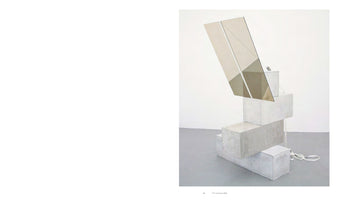 An abstract sculpture in a minimalist white room, featuring a precarious stack of four rectangular, light-gray concrete blocks. A large, two-panel, bronze-tinted mirror is propped at an angle on the top block, its surface reflecting fractured images of the gallery. A white nylon strap lies coiled on the gray floor near the base.