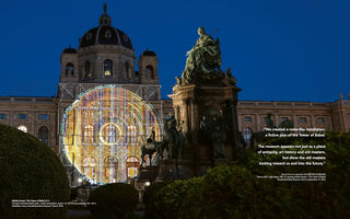 A night view of the Kunsthistorisches Museum in Vienna, a grand building with a domed roof, set against a deep blue sky. A large, circular, and colorful light installation with intricate geometric lines is projected onto the museum's facade. In front of the building stands an ornate monument with several bronze statues, and dark green bushes are visible in the foreground.