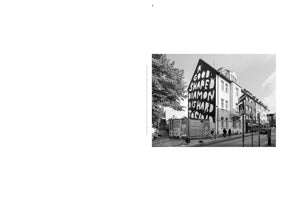 A black and white photograph of a city street corner. A large mural is painted on the side of an apartment building, featuring stylized white text on a black background that reads, A GOOD SHAPED DIAMOND IS HARD TO FIND. Pedestrians are visible on the sidewalk below.