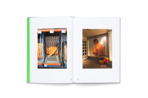 An open book with a grey cover and bright green spine detail laid flat on a white surface. The spread displays two photographs on pages 34 and 35. The left photo shows golden baguettes arranged in a metal store rack. The right photo shows a person wrapped in a vibrant orange blanket sitting inside a lit glass enclosure.