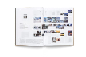 An overhead view of an open art book with a textured gray cover, resting on a white surface. The two-page spread displays German text and a grid of numerous small color images of paintings by Gerhard Richter, mostly featuring abstract and snowy mountain landscapes.