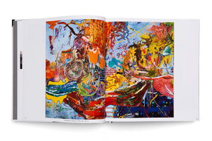 An open art book on a white surface displays a large, colorful abstract painting across the right-hand page. The artwork is a chaotic and vibrant mix of red, yellow, blue, and orange, featuring drips, swirls, and energetic brushstrokes. The book's dotted spine is visible on the left.