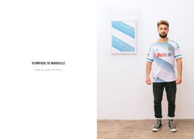 A man wearing an Olympique de Marseille soccer jersey stands in a white room next to a framed artwork hanging on the wall. The artwork is a painting with a pattern of diagonal light blue lines that perfectly matches the design on the man's jersey. The image is a composite, with text on the left side identifying the artwork as OLYMPIQUE DE MARSEILLE, Acrylic on canvas, 40 x 50 cm.