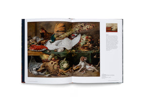 An open art book displays a large, opulent still-life oil painting from the Baroque period. The chaotic scene shows a table laden with a dead white swan, a peacock, a red lobster, fruit, and vegetables. On the floor below, a dead fawn lies near two snarling dogs.