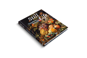An angled, high-view shot of a hardcover book titled Still Life, Timeless Beauty, on a plain white background. The black cover features a lush, classical still life painting of fruits, gourds, a bird's nest with eggs, and insects.