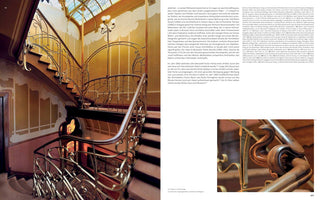 A two-page spread from a book showcasing an elegant Art Nouveau staircase. The main photo on the left displays the winding stairs with an ornate, gilded metal balustrade featuring whiplash curves, and a polished wooden handrail. The warm-toned walls are adorned with painted murals below a stained-glass skylight. The right page contains German text and a smaller inset photo with a close-up of the intricately carved wooden handrail.