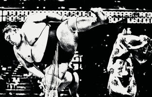 A grainy, high-contrast black-and-white photograph captures a sumo wrestler in a dynamic pose. He is bent forward, raising one muscular leg high into the air in a ritual stomp. In the background, a referee in a patterned robe and a digital scoreboard are partially visible.