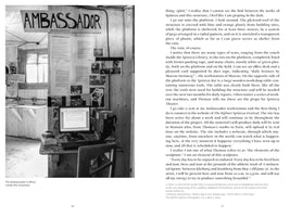 A black and white book spread. The left page features a photograph of a rustic, makeshift office inside a wooden structure. A hand-painted sign reading AMBASSADOR hangs on the wall above a desk with an old computer, with papers and smaller photos pinned around it. The right page contains a full page of text.