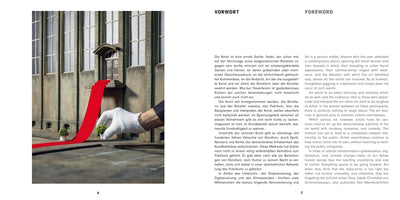 An open book spread shows its foreword in German and English. The left page features a photograph of a hand in a white glove setting up a miniature scene, placing a tiny potted plant beside a red carpet that leads up to the entrance of a model building.