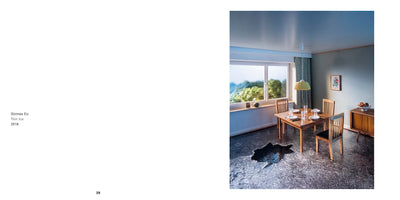 A two-page book spread. The left page lists the title, Dünnes Eis, Thin Ice, and the year, 2018. The right page is a photograph of a dining room with a wooden table set for a meal by a large window overlooking a green landscape. On the dark, mottled floor, there is a jagged black shape that looks like a hole or an animal hide.
