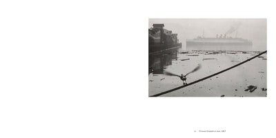 A black and white photograph from 1957 of a foggy harbor. In the foreground, a bird with motion-blurred wings perches on a thick mooring line stretched over debris-filled water. In the background, the large ocean liner Princess Elizabeth or Joan is visible through the mist, with buildings lining the shore to the left.