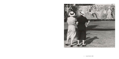 A black and white photograph from 1960 titled English Bay (2). Two women are seen from behind, standing on a sunny lawn. Both wear dresses and white hats as they look at a large mural depicting a bustling historical parade with horse-drawn carriages and people in vintage clothing.
