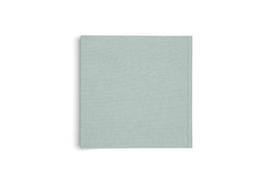 A top-down view of a closed hardcover book with a light sage-green, linen-textured cover, set against a plain white background with a subtle shadow.
