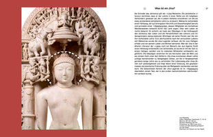 A book page showing a large, intricately carved white marble statue of Jina Rishabha from 11th-12th century India. The figure has a serene expression with closed eyes and is framed by an elaborate arched backplate crowded with many smaller figures, attendants, and elephants. To the right is a column of German text titled Was ist ein Jina?