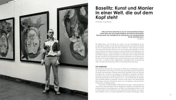 A black and white photograph from a book shows the artist Georg Baselitz in a gallery. He stands next to his large, expressive paintings, which famously depict portraits hanging upside down. The photo is part of a two-page spread with German text on the right.
