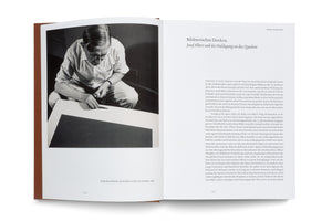An overhead shot of an open book. The left page features a black-and-white photograph of the artist Josef Albers leaning over a canvas, applying paint with a palette knife. The right page contains an essay written in German.