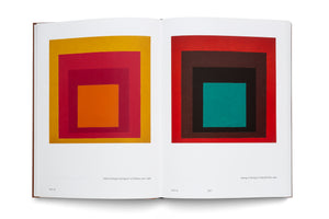 An open art book showing a two-page spread of Josef Albers' Homage to the Square paintings. The left page displays a piece with concentric squares in warm tones of yellow, red, and orange. The right page features a similar composition with an outer red square, dark inner squares, and a teal center.