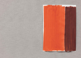 An abstract, top-down photograph of a light gray, textured fabric background. On the right side, a piece of white paper is painted with a thick, vertical stripe of bright orange next to a thinner stripe of dark reddish-brown.