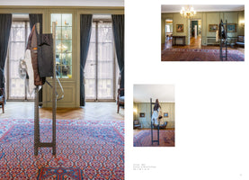 A page layout displaying three photos of an art installation in a classically decorated room. A tall, industrial-style perforated metal coat rack with several garments hanging on it stands on a colorful, patterned Persian rug. The elegant room features light green walls, herringbone wood floors, and large windows with dark curtains. Two smaller photos on the right show the installation from different viewpoints.