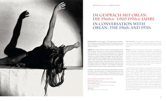 A page from a book featuring an interview with the artist ORLAN. On the left is a dramatic black-and-white photograph from her 1967 performance Body-sculpture No. 6. It shows a woman in an arched pose on a surface, her arms raised and a dark shadow cast on the wall behind her. The right side has the title IN CONVERSATION WITH ORLAN: THE 1960S AND 1970S, followed by the interview text in German and English.