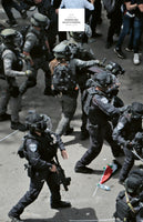 An overhead, slightly blurred photo shows Israeli police in full tactical riot gear, including helmets and vests, advancing on a street. A Palestinian flag lies on the ground near their feet. A white text box in the upper portion of the image reads: ASIA SINGLES SHIREEN ABU AKLEH'S FUNERAL MAYA LEVIN.
