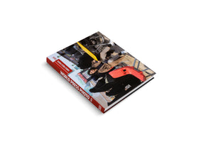 The World Press Photo 2023 hardcover book, shown at an angle on a white background. The book has a red spine with the title in white. The cover features a rotated photograph of a woman in a tan coat looking up at the camera amidst urban debris.