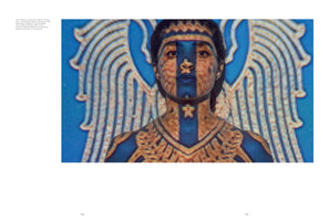 A still from a video installation showing a woman's face and shoulders as she looks directly at the viewer. A colorful, pixelated image is projected onto her and the background. A wide, vertical blue stripe runs down the center of her face, and a golden, ornate pattern covers her chest like a collar. Behind her, the projection creates a pair of large, stylized wings against a bright blue background.
