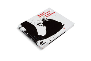 An angled, overhead view of the hardcover art book Robert Motherwell Pure Painting on a white surface. The book's white cover features a large, abstract, gestural black painting and the title in bold red text in the upper right corner. The spine is also visible.