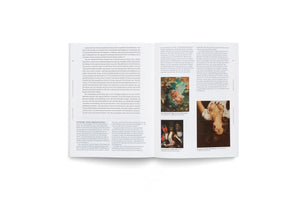 A high-angle shot of an open book lying on a white surface. The two-page spread contains German text in a multi-column layout and features several color images of various paintings.