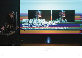 A musician wearing headphones and glasses performs with a guitar and electronic equipment on a dark stage. Behind them, a large screen displays a colorful, glitchy background with two images of a chrome-like cyborg and large white text that reads I HAVE TO WAKE UP, STOP THINKING AND MAKE LOVE WITH MY SOCIAL NETWORKS... I MAKE LOVE WITH THE POLITICAL SOCIETY OF THE SPECTACLE.