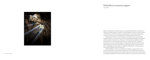 A two-page spread from a publication. On the left, a vertical photograph shows the inside of a dark, rocky cave, with several beams of bright sunlight streaming down from an opening in the ceiling. On the right, there is a body of text in Spanish, with the headline Profundizar en nuestros orígenes.