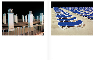 A two-page book spread with two nighttime photographs. The left page shows a concrete rooftop with several white, modern pillars under a black sky. The right page shows a sandy beach filled with numerous empty blue lounge chairs arranged in neat, receding rows.