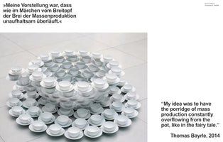 A high-angle photograph of Thomas Bayrle's art installation, Tassenfasse. The piece is a large, circular, tiered sculpture on a tiled floor, constructed from many identical white teacups and saucers stacked to look like an overflowing fountain. The image includes text in both German and English, featuring a quote from the artist explaining the work as a representation of the overflowing porridge of mass production, like in a fairy tale.