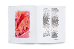 An open art book on a white surface. The left page shows a glossy, translucent sculpture in shades of pink and orange, compressed into a wrinkled block, identified as César, Compression, 1970. The right page contains a block of text in two columns, one in English and one in German.