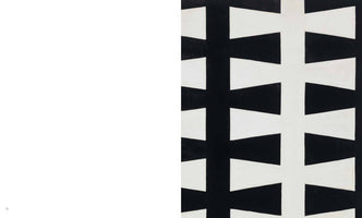 A page from a book showing an abstract black and white painting on the right side. The painting features a repeating geometric pattern of two vertical columns of white, cross-like shapes against a black background. The left page is blank and white.