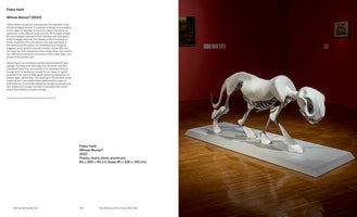 A page from an art catalog featuring Flaka Haliti's sculpture, Whose Bones?. The right side shows the sculpture in a gallery with red walls: a large, white, skeletal figure of a four-legged predator in a low, stalking pose. A smooth, stylized white form covers its head, back, and feet, while its metallic ribcage and leg bones are exposed. The left side of the page contains descriptive text about the artwork.