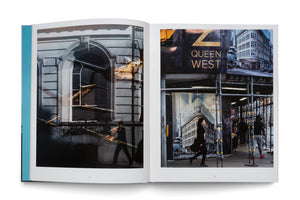 An open photobook with a teal spine displaying a two-page spread. The left page shows a black-and-white photo of a building facade with superimposed reflections of a golden-lit airplane. The right page shows a color photo of a city street scene with a sign for Queen West, scaffolding, and people walking on the sidewalk.