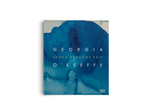 The square cover of the book Georgia O'Keeffe: Sehen braucht Zeit. The cover features an abstract watercolor design in various shades of blue. The title is printed in the center in a white, sans-serif, all-caps font. The publisher's logo, Hatje Cantz, is in the bottom right corner.