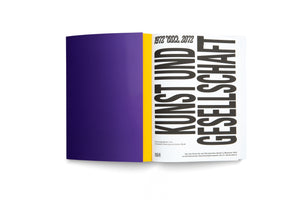 A book with a solid purple cover and a bright yellow spine stands upright against a white background. The book is slightly ajar, showing the title page with the words KUNST UND GESELLSCHAFT in a large, bold, black font, beneath the years 1972 2022 2072.