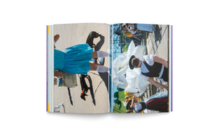 An open book on a white background displays a two-page spread with sideways photographs. The left page shows a high-angle shot of a person in a bright blue dress and white socks walking a small black dachshund on a sunny pavement. The right page captures a festival scene with people in traditional German-style clothing near large, white inflatable sculptures.