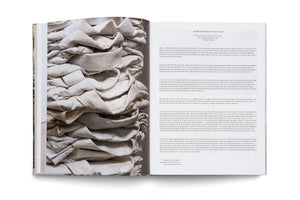An open book viewed from above. The left page is a full-bleed photograph of a stack of folded, off-white fabric stiffened with a chalky substance. The right page features the prose poem Immigrant Haibun by Ocean Vuong, with black text on a white background.