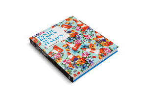 A hardcover book titled Textil Design aus Italien, displayed at an angle on a white background. The cover features a busy, colorful pattern of various flowers mixed with orange and white striped traffic cones on a light blue field. The title is presented in blue text within a white box. The book has a black spine and bright blue page edges.