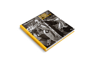 A square hardcover book with a bright yellow spine, titled Picasso, Friends and Family by Edward Quinn. The cover features a black-and-white photograph of an older man, likely Picasso, smiling warmly while wearing a heavy coat and a hat with two pigtail braids. The book is angled on a plain white background.