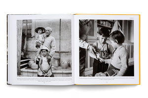An open book with a yellow spine is laid flat, showing a two-page spread with black-and-white photographs. The left page features a photo of Pablo Picasso holding his daughter Paloma, with his son Claude standing in front of them. The right page shows Picasso presenting a small, framed photo of himself as a child to his two children.