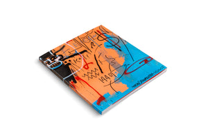 An angled, three-quarter view of a hardcover art book on a white background. The cover features a vibrant and chaotic neo-expressionist painting in the style of Jean-Michel Basquiat. The artwork is a mix of bright orange and blue, overlaid with black, red, and white graffiti-style markings, symbols, and text.