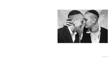 A black and white photograph, titled Kindred Spirits, 1994, is set against a white background. It shows two people with shaved heads, each wearing a yarmulke, in a close and tender embrace. They are face-to-face, foreheads and noses nearly touching. One person's hand rests gently on the back of the other's head. Both are wearing dark jackets over white collared shirts.