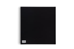 A top-down photo of the back of a solid black hardcover book, set against a white background. In the bottom-left corner, there is a small white sticker with a barcode, ISBN number, and a website address.